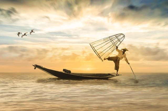 Fisherman on the edge of a boat balancing between a pole and a net.