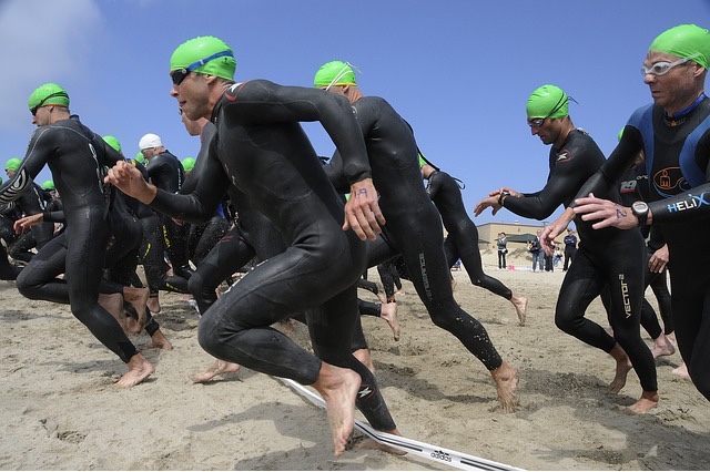 swimmers in green caps running into the water at the start of a race. 