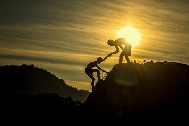 One person helping another climb a mountain