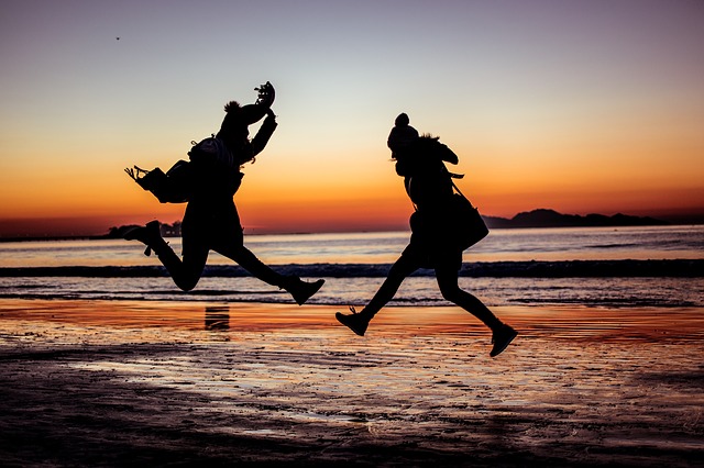 Two people jumping on a beach in the sunset
