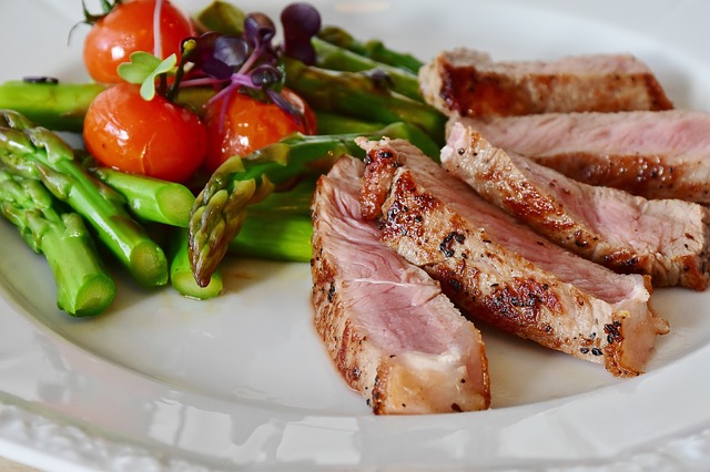 plate of dinner with nicely cooked meat, asparagus, tomatoes. 