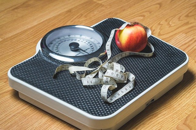 A scale with a measuring tape and apple. 